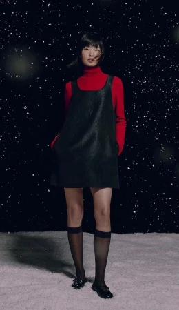 Model Jing Huang in a black pinafore dress and red turtleneck standing against a snowy starry backdrop for Marc O'Polo.