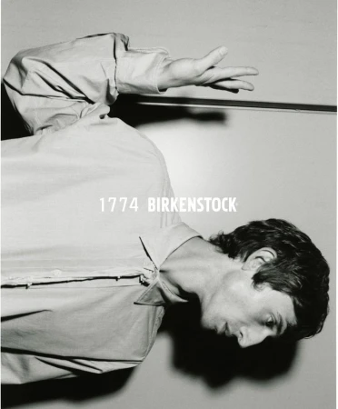 Monochromatic portrait of a man in a light-colored, long-sleeved shirt, facing right with raised hand and '1774 BIRKENSTOCK' text overhead.
