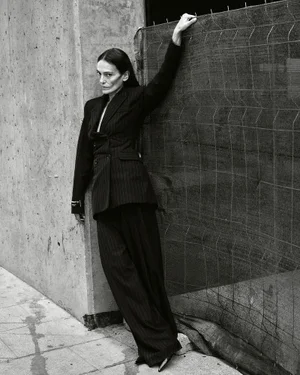 Model wearing dark pinstripe suit leaning against a concrete wall outdoors