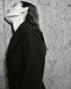 Black and white side profile of Laura Ponte in a dark pinstripe blazer leaning against a textured concrete wall.