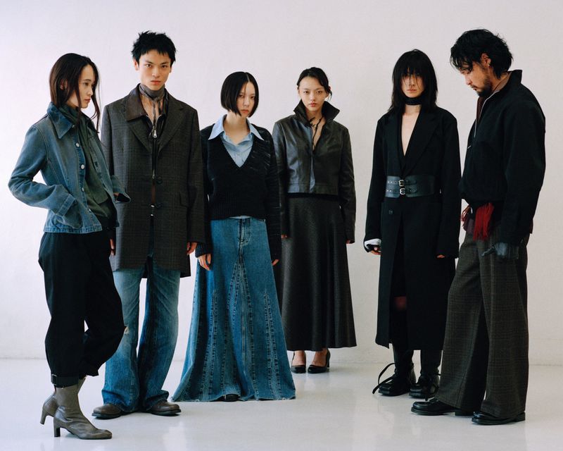 Six diverse adults in a white studio showcasing denim and tailored pieces in a fashion editorial with studio lighting and a neutral backdrop.