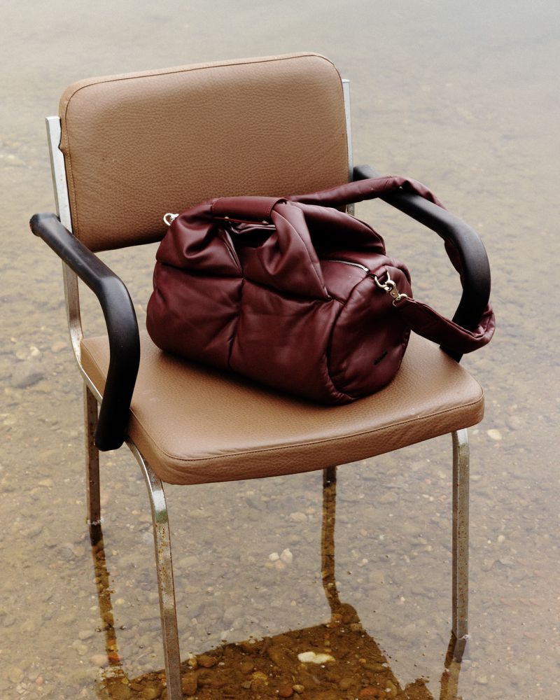 Burgundy quilted leather handbag resting on a tan upholstered vintage chair standing in shallow natural water.