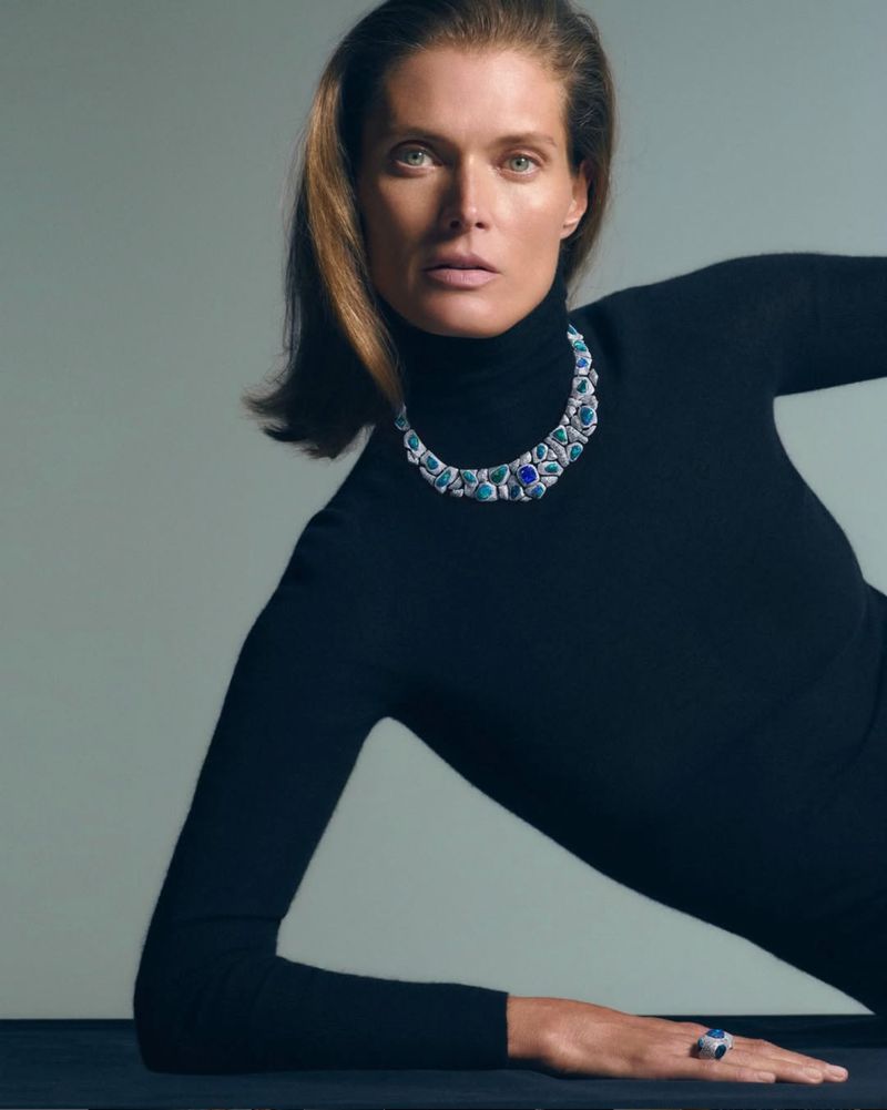 Portrait of a woman with auburn hair wearing a black turtleneck, ornate necklace, and ring while posing in a photography studio.