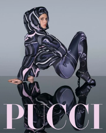 Woman poses in patterned puffer jacket and leggings with matching high heels on reflective surface, promoting fashion brand Pucci.