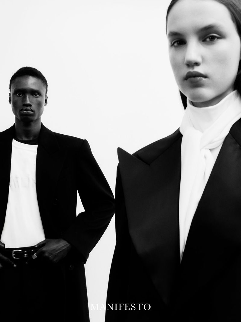 Black and white fashion shot featuring a woman in a black blazer with a white scarf and a man in a black blazer and white t-shirt.