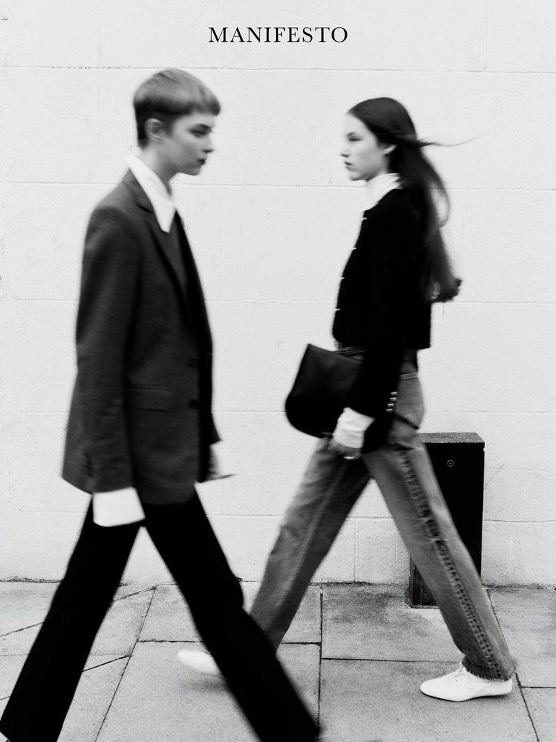 Two fashion models walk on a city street in a black and white editorial shot with 'Manifesto' text overlay.