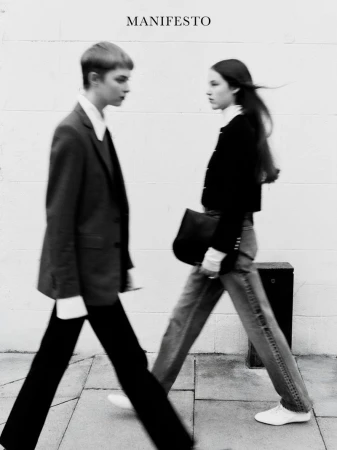 Two fashion models walk on a city street in a black and white editorial shot with 'Manifesto' text overlay.