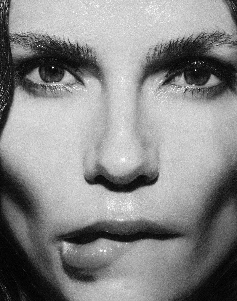 Close-up black and white portrait of an adult woman with dark hair and light skin, her eyes prominent, biting her lip.