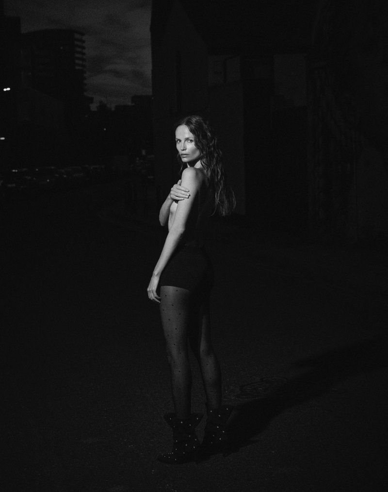 Black and white portrait of a female adult in black clothing and studded boots in an urban outdoor environment at night.