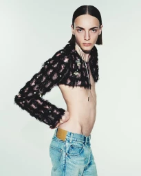 Model with slicked-back dark hair wearing a black textured cropped jacket and blue denim jeans against a white background