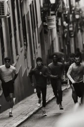Black and white photo of five men running down a narrow city street wearing athletic shorts, shirts, and running shoes.