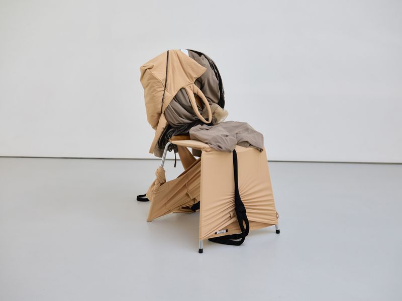 Chair draped with beige and gray fabric in front of a white wall, minimalist and modern aesthetic.