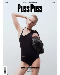 Model Hannah Motler posing in a black swimsuit holding a patterned handbag against a white seamless background for Puss Puss Magazine