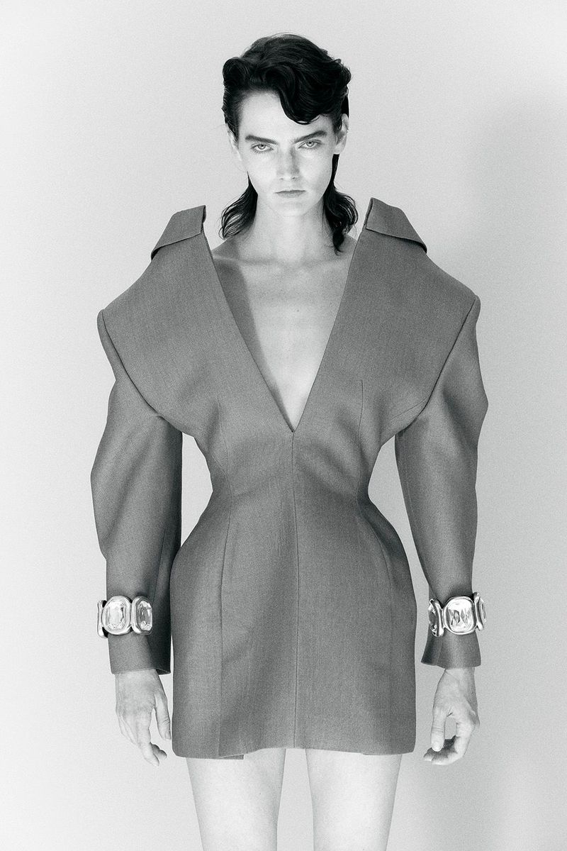 Monochrome studio shot of a woman with dark hair in a gray couture dress with silver cuffs, captured in a portrait orientation.