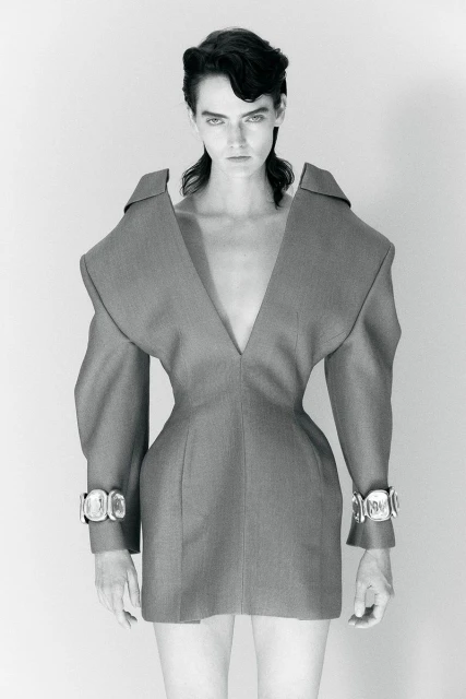 Monochrome studio shot of a woman with dark hair in a gray couture dress with silver cuffs, captured in a portrait orientation.