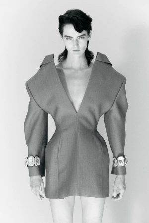 Monochrome studio shot of a woman with dark hair in a gray couture dress with silver cuffs, captured in a portrait orientation.