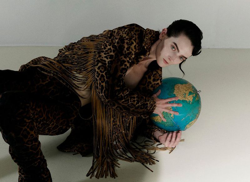 Man in a leopard-print suit poses while holding a globe in a studio setting, showcasing a blend of fashion and surreal imagery.