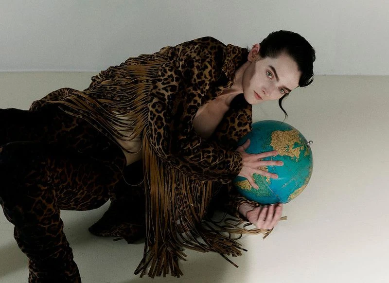 Man in a leopard-print suit poses while holding a globe in a studio setting, showcasing a blend of fashion and surreal imagery.