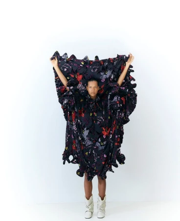 Model Brooke Gabel holding up an oversized black floral ruffled dress against a plain white studio background.