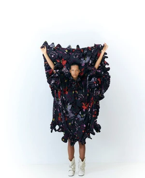 Model Brooke Gabel holding up an oversized black floral ruffled dress against a plain white studio background.