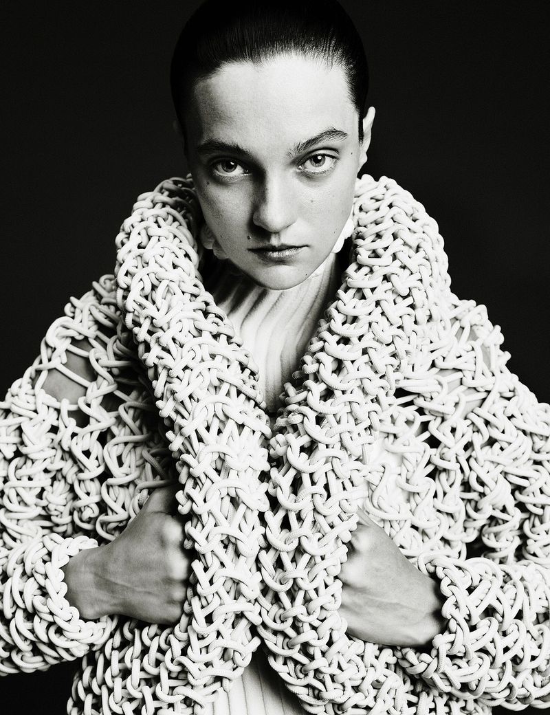 Monochrome portrait of an adult female with short dark hair wearing a white knit jacket. Direct eye contact on a dark background.