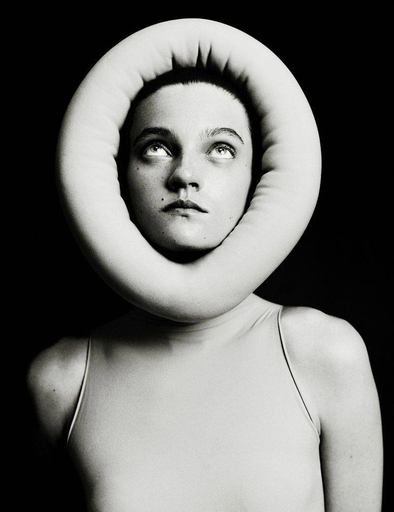 Headshot of a young adult female with fair skin, staring upwards. She is framed by a large, soft, ring-shaped object in a photo studio.