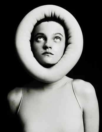 Headshot of a young adult female with fair skin, staring upwards. She is framed by a large, soft, ring-shaped object in a photo studio.