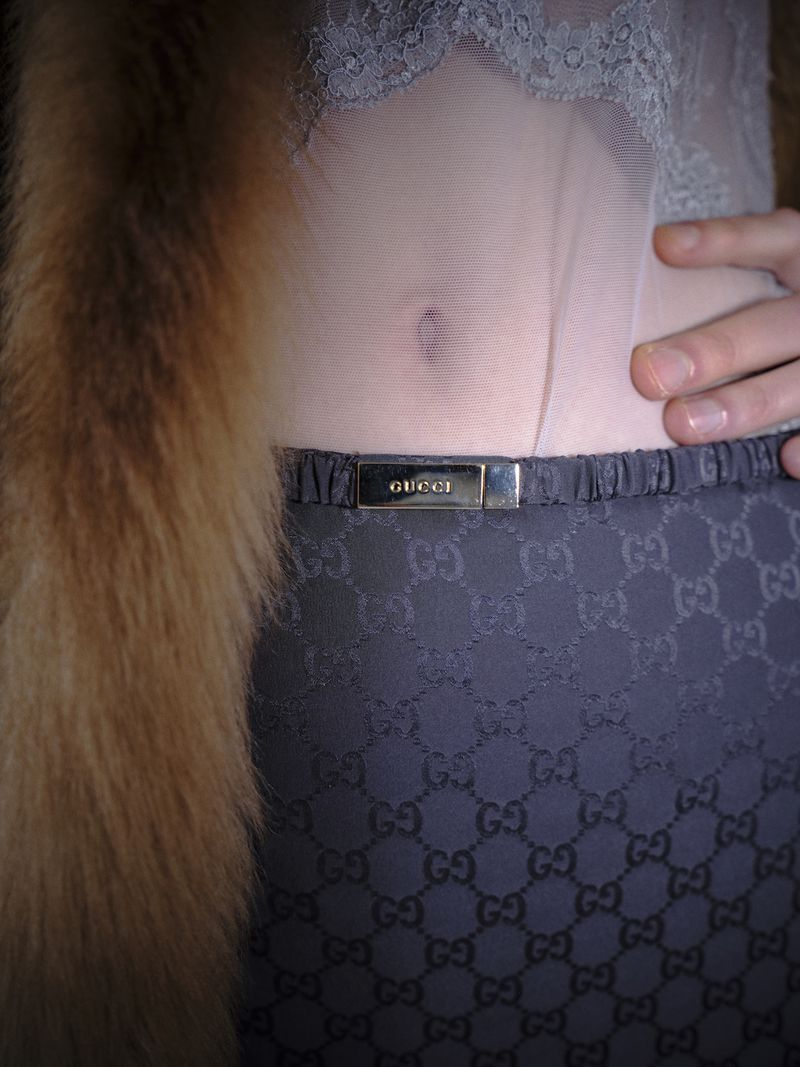 Fashionable image features a person wearing a Gucci belt with monogram skirt, lace top, and fur stole, emphasizing high-end style and design.
