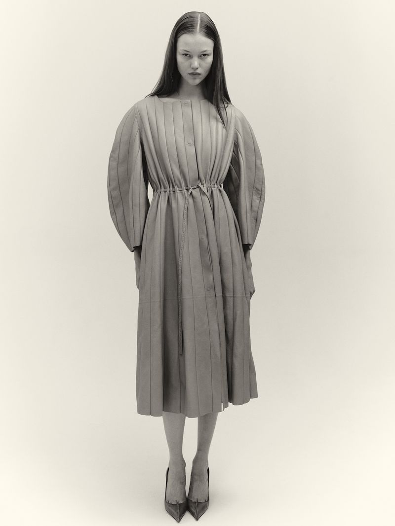 A full shot presents a single, straight-haired model in a vertically striped dress and heels against an off-white backdrop, studio lighting.