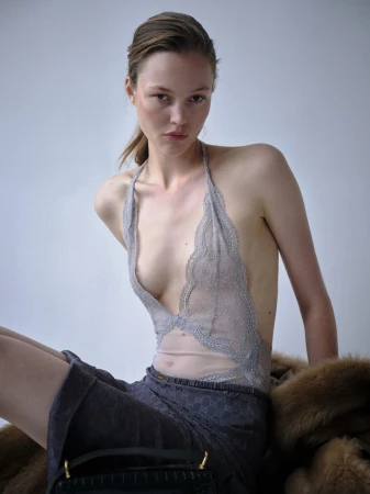 Fashion shot of a young woman wearing a light blue lace bodysuit and a dark blue skirt with a fur shawl and handbag in the foreground.