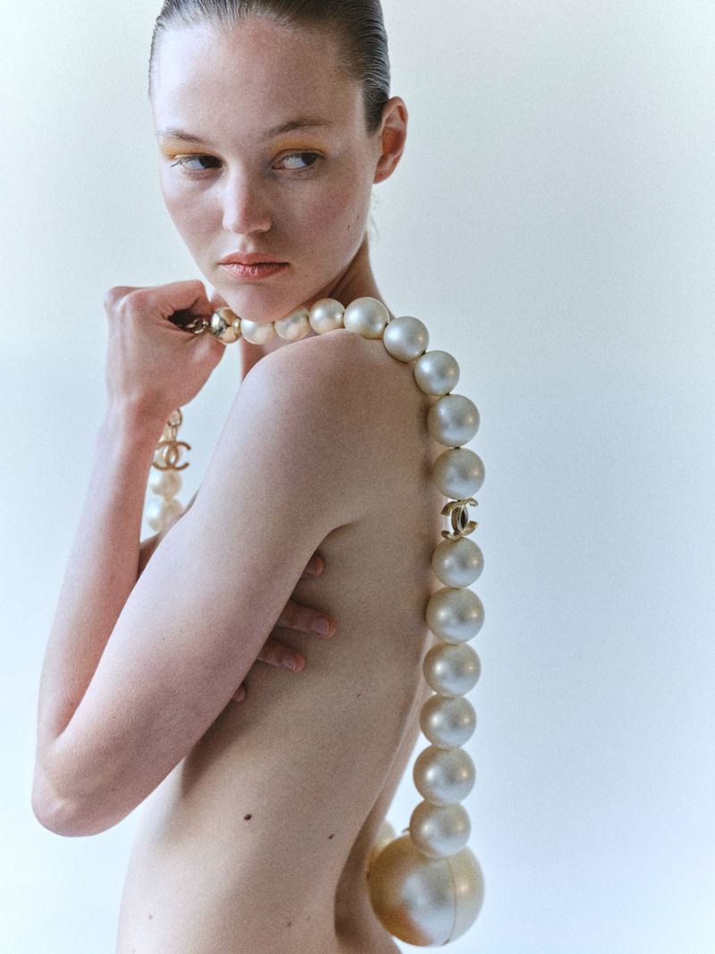 Model wearing an oversized pearl necklace draped over her shoulder against a plain white background for Manifesto Magazine.
