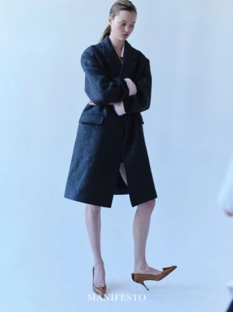Model standing against a white backdrop wearing a long dark wool coat and brown pointed heels