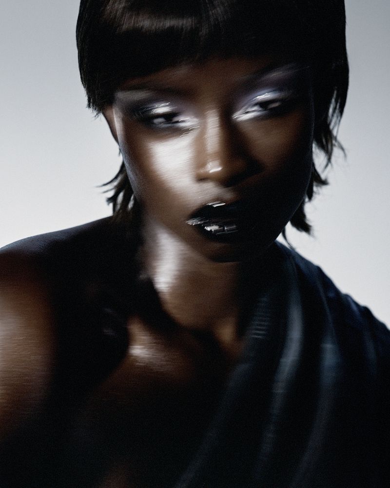 Fashion portrait of an adult female with dark skin, metallic eyeshadow, and glossy black lips. Close-up shot, studio lighting.