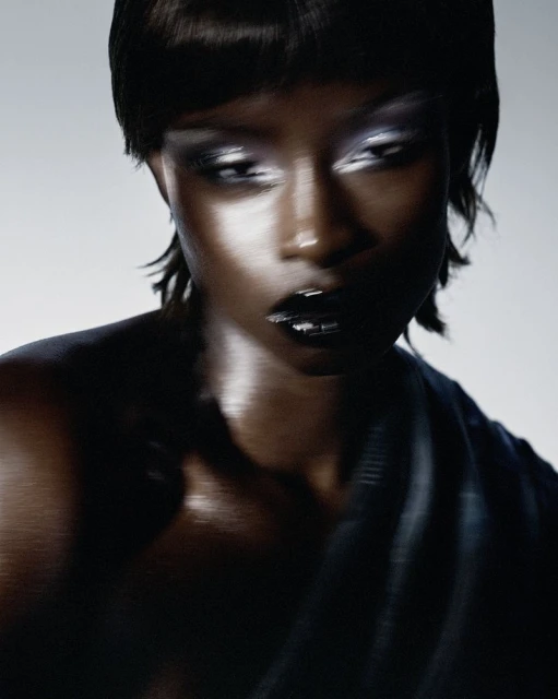 Fashion portrait of an adult female with dark skin, metallic eyeshadow, and glossy black lips. Close-up shot, studio lighting.