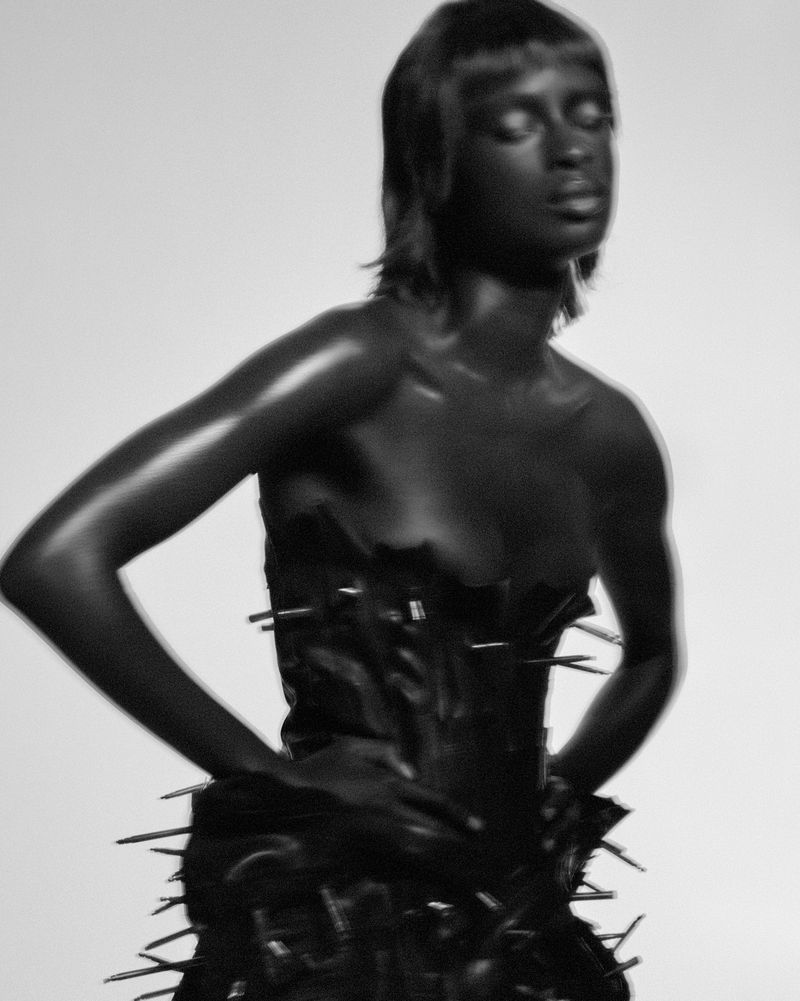 Monochrome fashion portrait of a Black woman with short hair wearing a black dress with metal spikes in a photo studio setting.