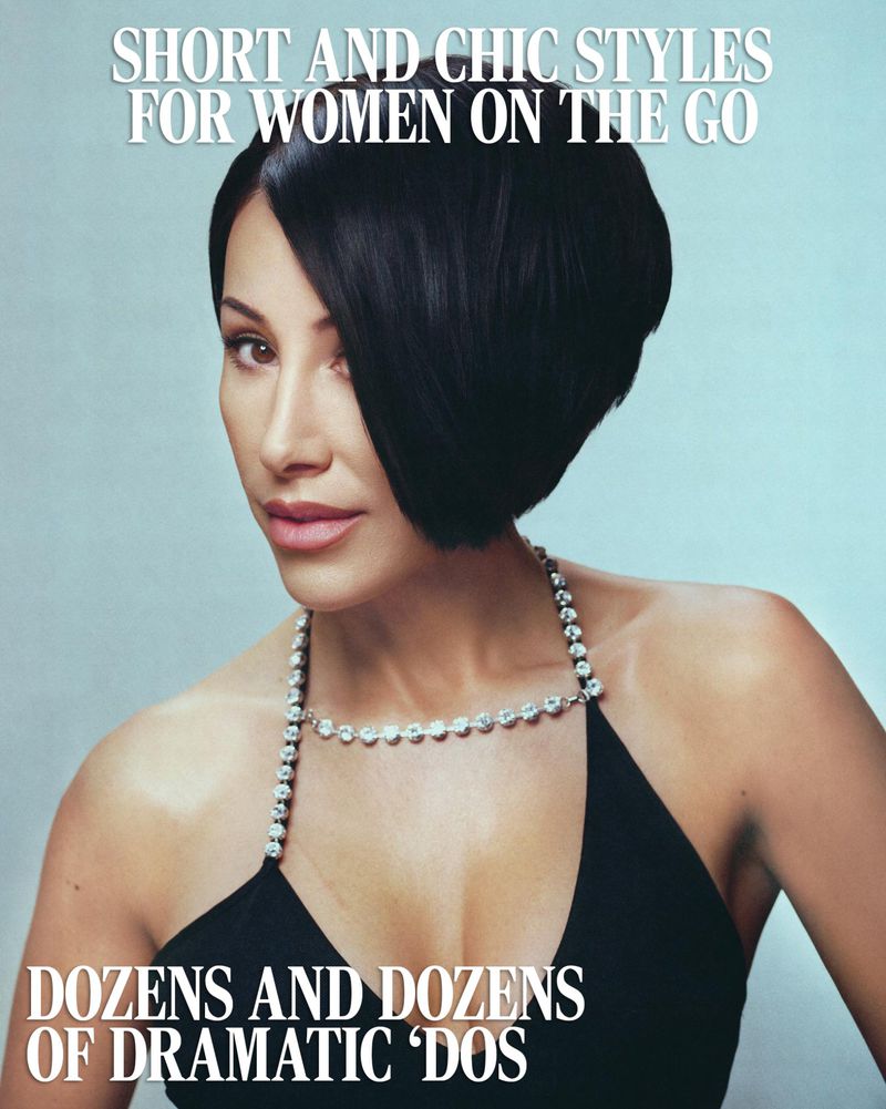 Close-up of a woman with a black asymmetrical bob hairstyle, wearing a black halter top and diamond necklace, against a light blue background.