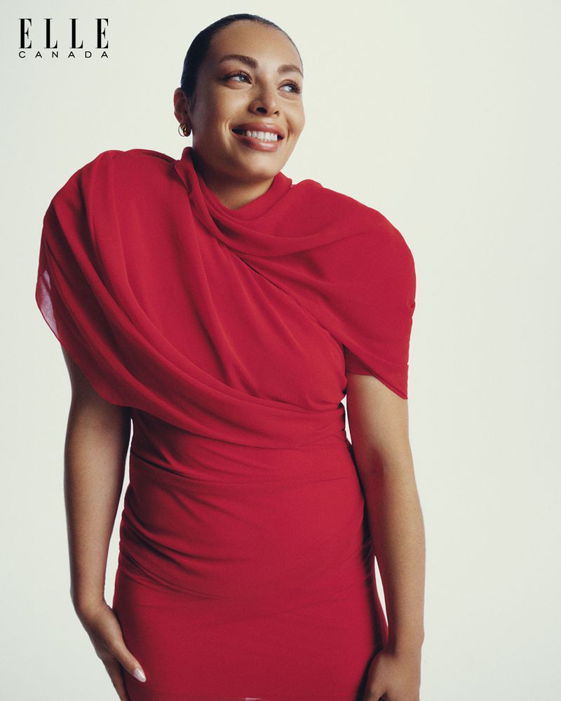 Portrait of woman in red dress looking to the side with a slight smile, against a white background for an Elle Canada photoshoot.