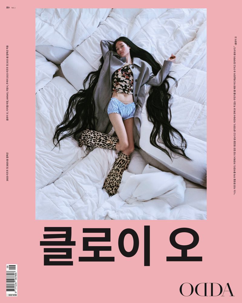 Magazine cover features a model in a corset top, shorts, coat, and leopard-print boots lying on a white comforter with pink background.