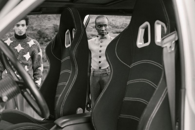 Monochrome shot inside of a vehicle focusing on the front seats with two people visible in the background in an outdoor setting.