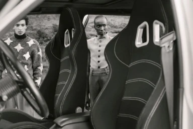 Two fashion models viewed through the sport bucket seats of an open car in a black and white editorial shoot.