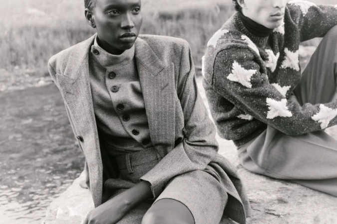 Black-and-white fashion editorial image featuring two models outdoors wearing structured wool tailoring and patterned knitwear.