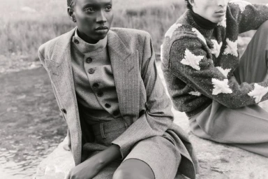 Black-and-white fashion editorial image featuring two models outdoors wearing structured wool tailoring and patterned knitwear.