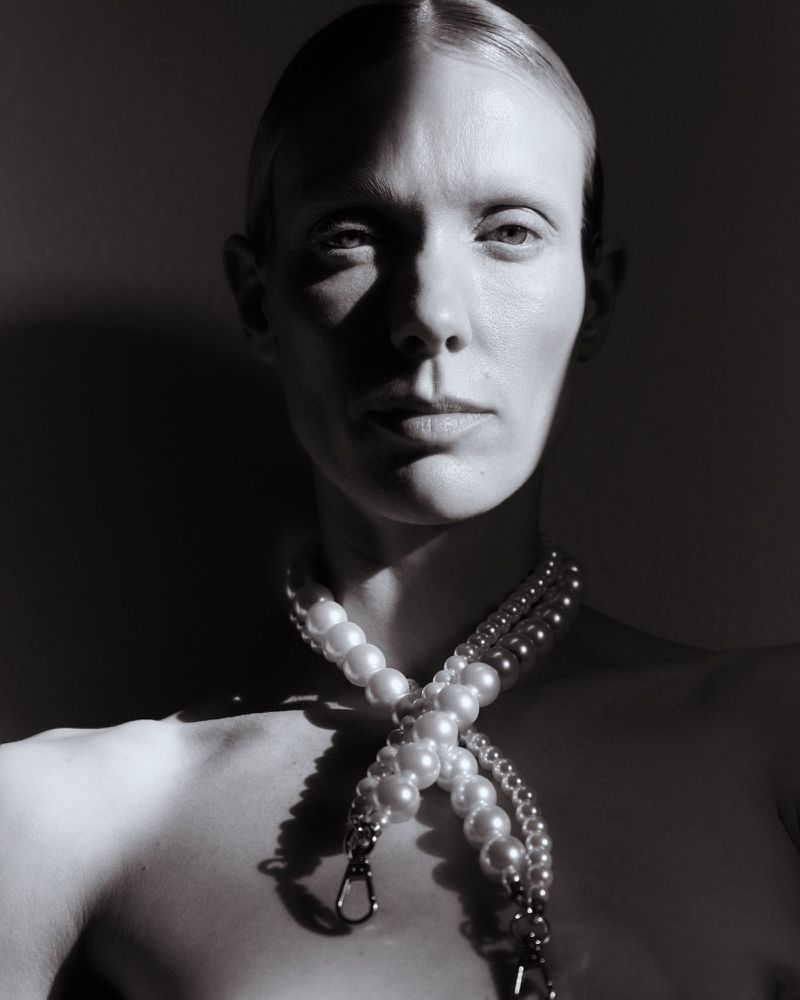 Striking black and white portrait of a woman with a pearl necklace, showcasing dramatic chiaroscuro lighting and elegant composition.