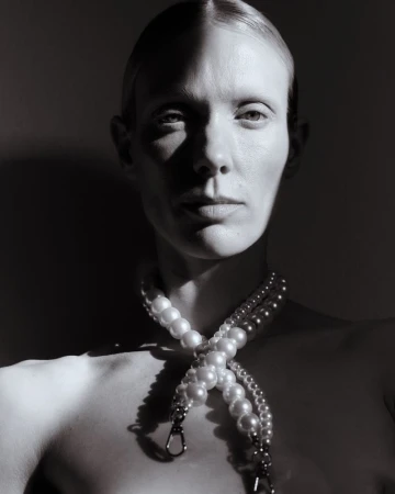 Striking black and white portrait of a woman with a pearl necklace, showcasing dramatic chiaroscuro lighting and elegant composition.
