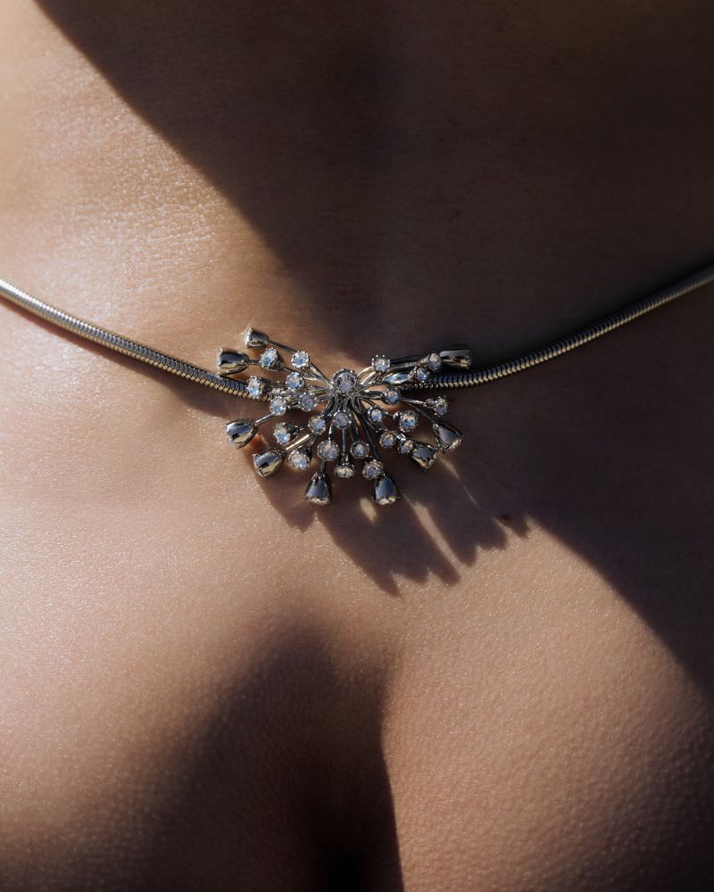 Close-up of a silver gemstone pendant necklace worn on a person's chest under bright hard lighting.