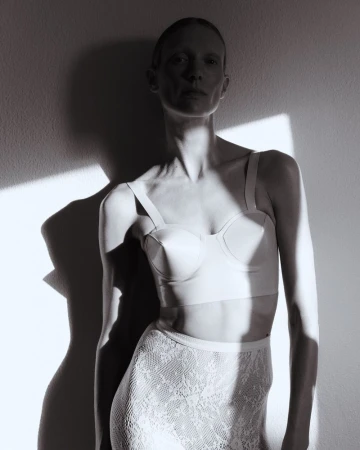 Model Annely Bouma wearing lingerie and lace skirt against a wall in dramatic light for Duel Magazine.