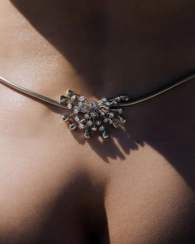Close-up of a silver gemstone pendant necklace worn on a person's chest under bright hard lighting.