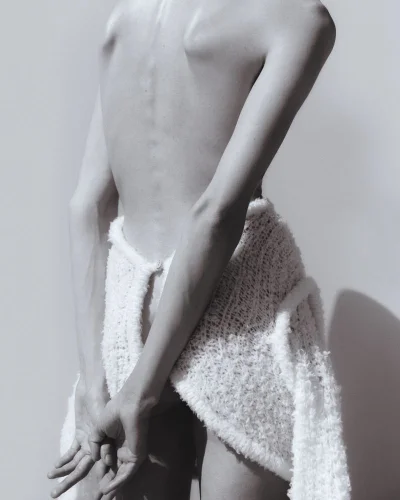 Back view of model Annely Bouma wearing a textured white knit skirt against a pale studio background.