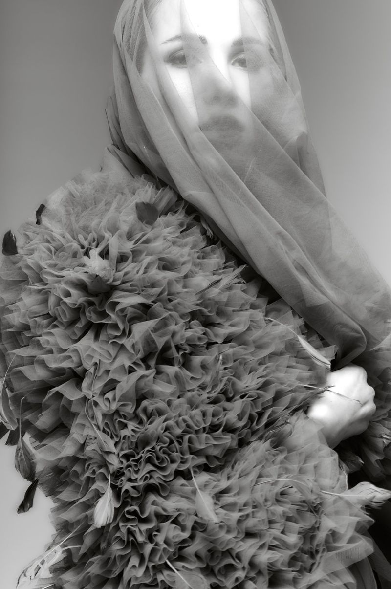 Portrait of woman with tulle veil and ruffled collar in a black and white photograph. Fashion editorial with ruffles and feathers.
