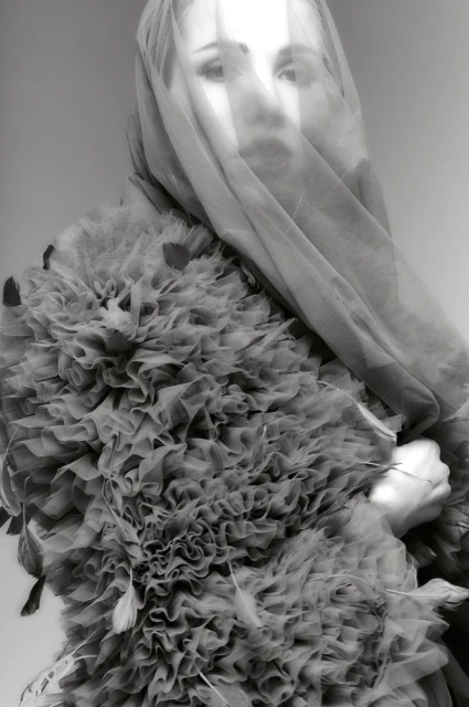 Portrait of woman with tulle veil and ruffled collar in a black and white photograph. Fashion editorial with ruffles and feathers.